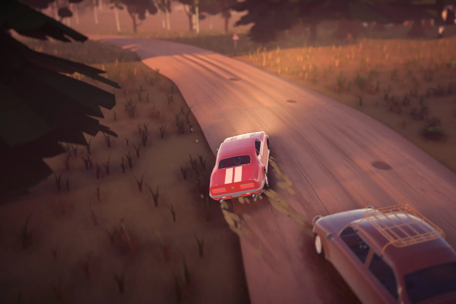 Low behind two coupes racing nose to tail down a dusty road at dusk