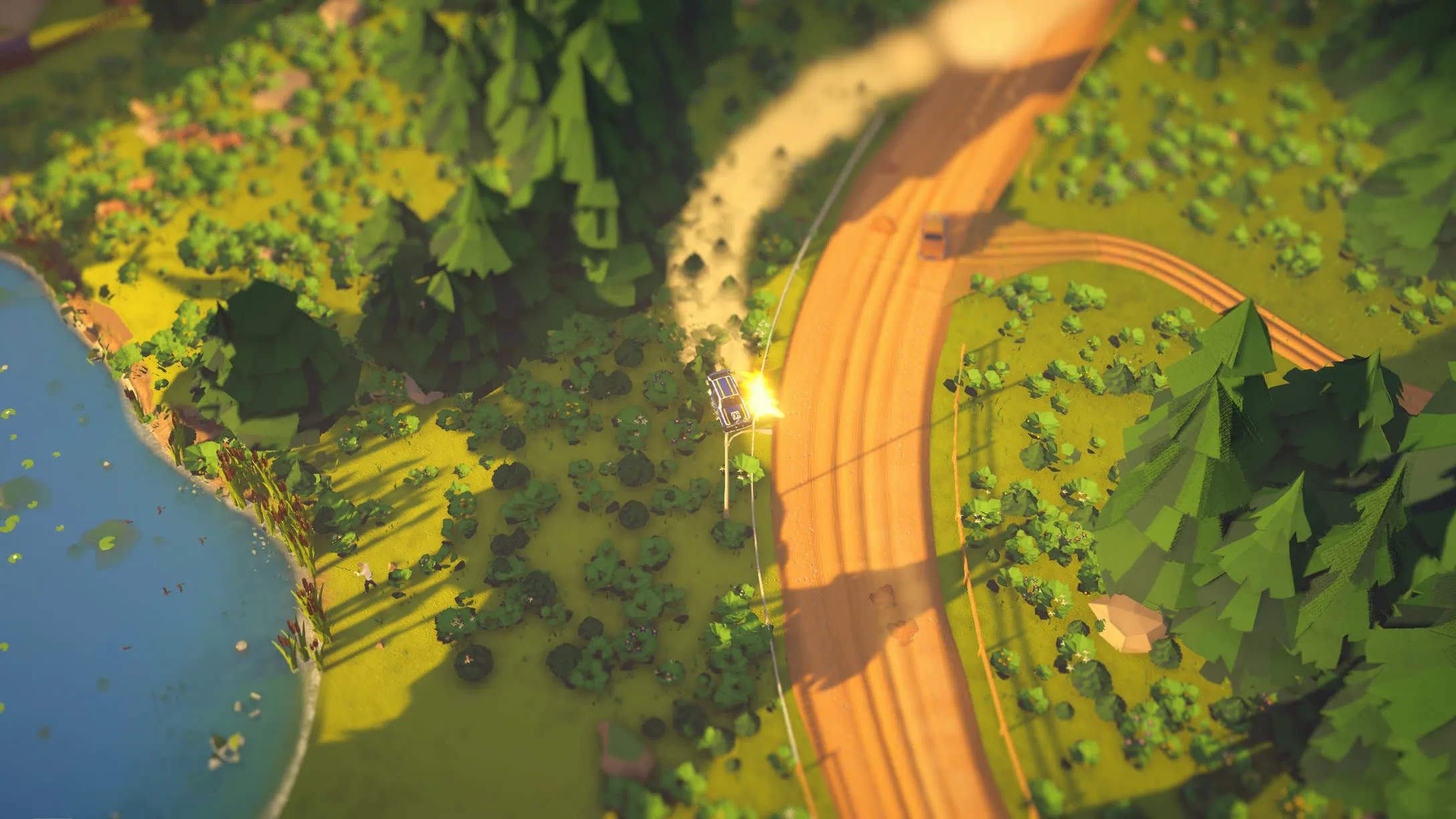 From high above: a car drifting through a gravel S-bend beside a lake in low evening sun, a plume of dust behind it