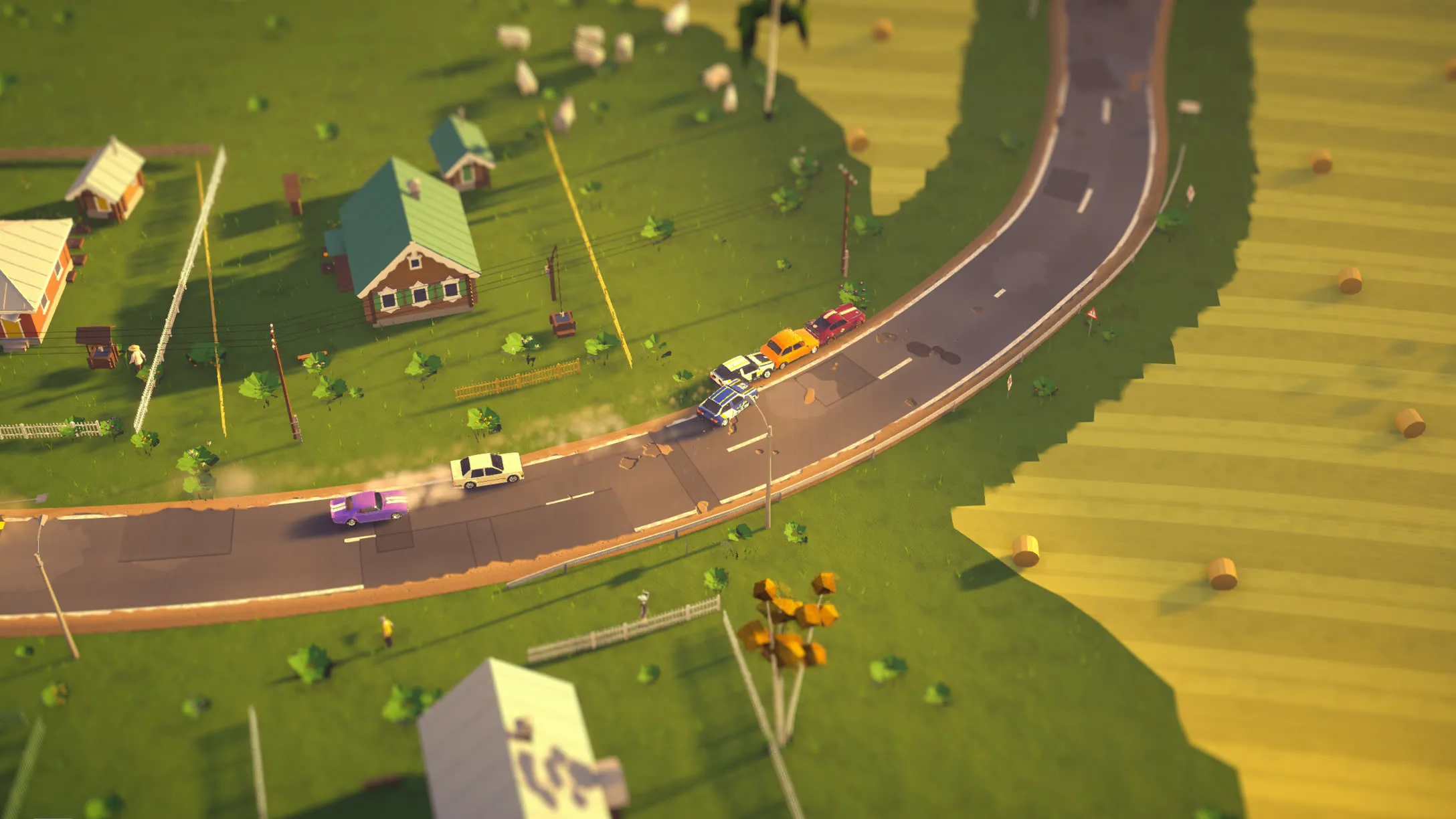 A village road winding between farmhouses and golden fields, the field of cars strung along it